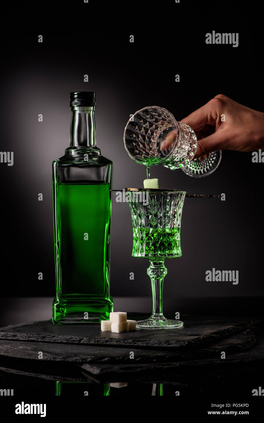 cropped shot of woman pouring absinthe in glass and on sugar cube on dark background Stock Photo
