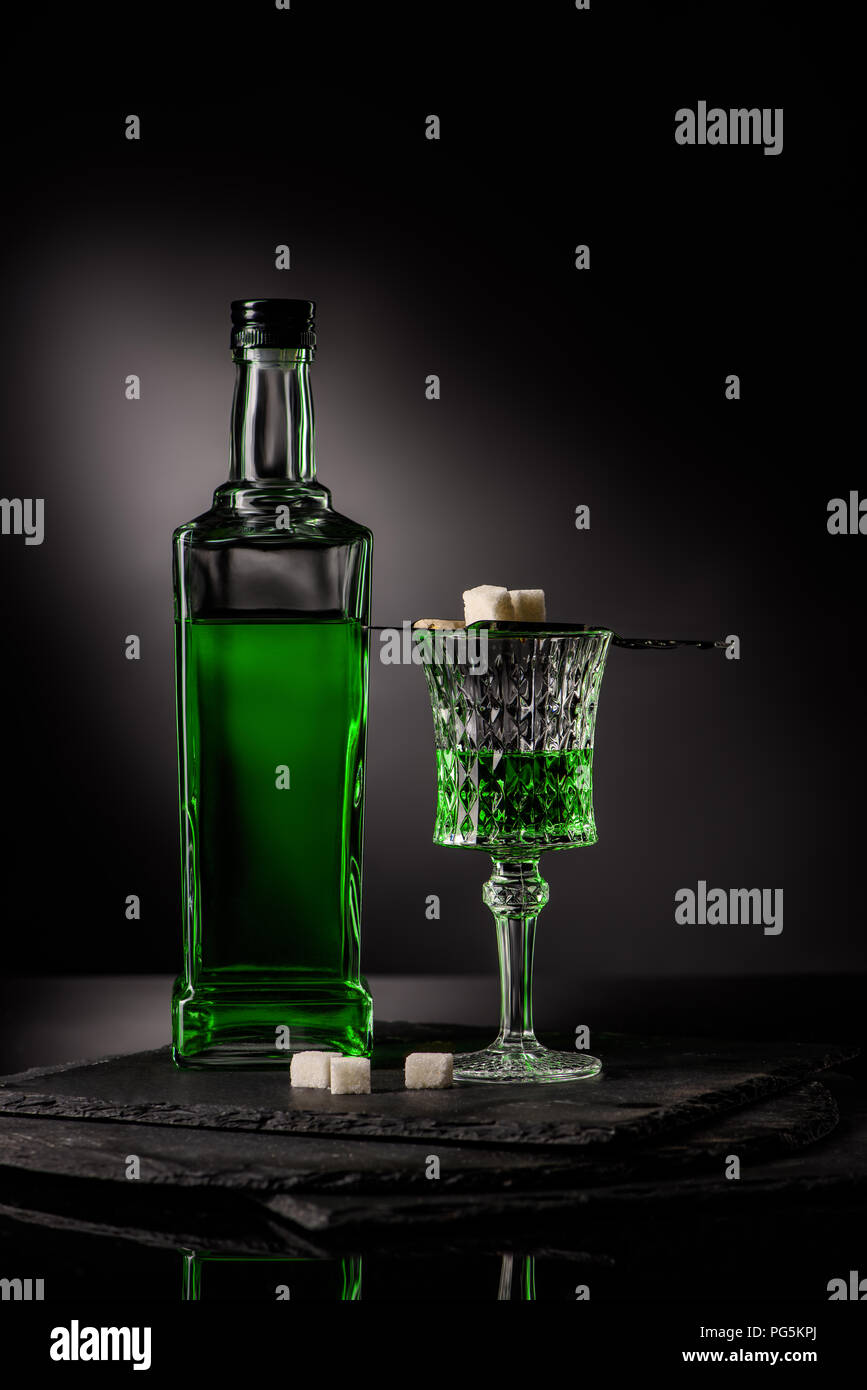 close-up shot of glass and bottle of absinthe with spoon and sugar cubes on dark background Stock Photo