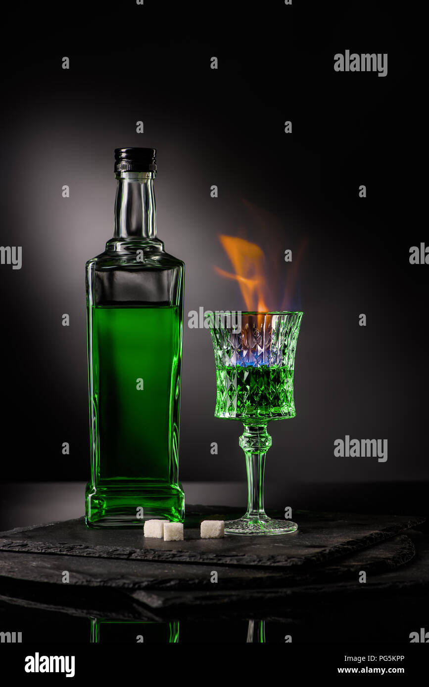 close-up shot of bottle and glass of burning absinthe on dark background Stock Photo