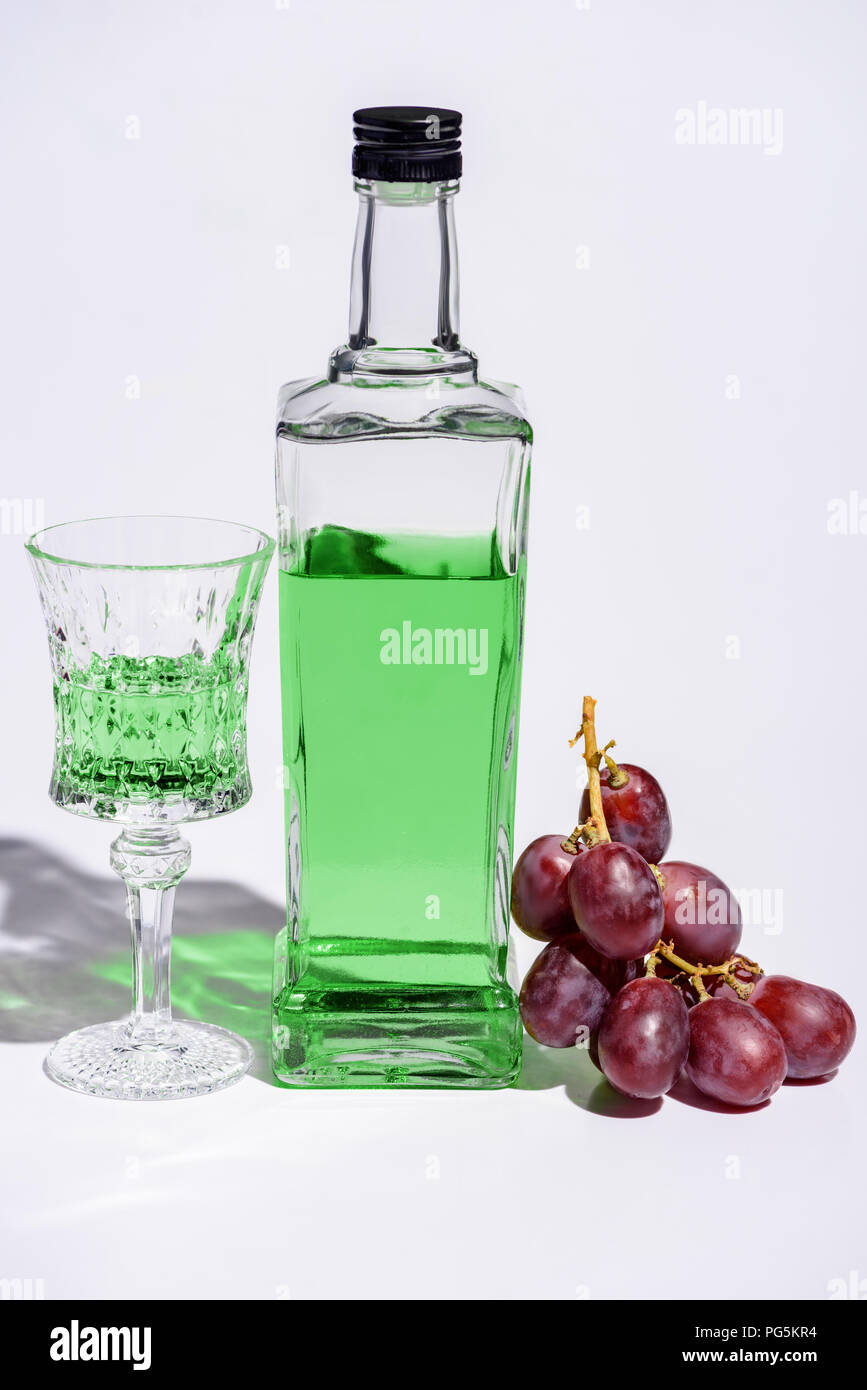 crystal glass and bottle of absinthe with branch of grapes on white Stock Photo