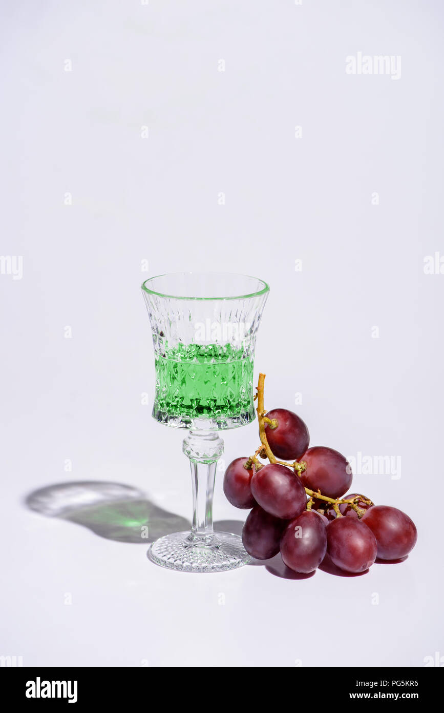 crystal glass of absinthe with branch of grapes on white Stock Photo
