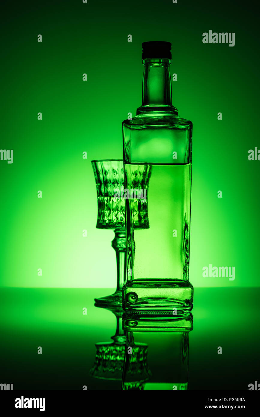 bottle of absinthe with lead glass on mirror surface and dark green background Stock Photo