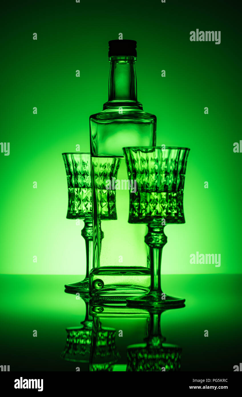 bottle of absinthe with lead glasses on mirror surface and dark green background Stock Photo
