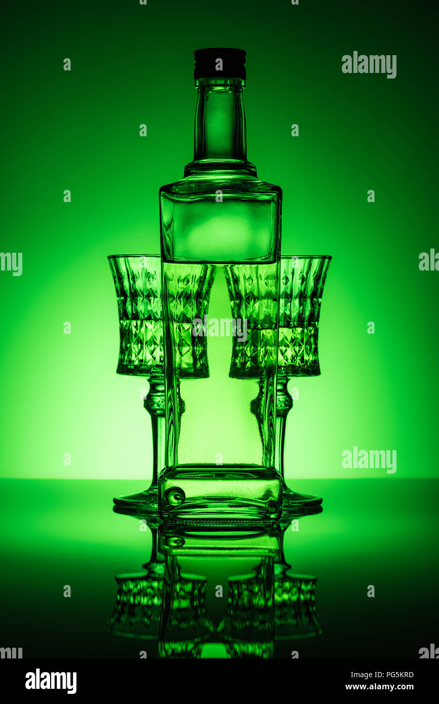 bottle of absinthe with crystal glasses on mirror surface and dark green background Stock Photo