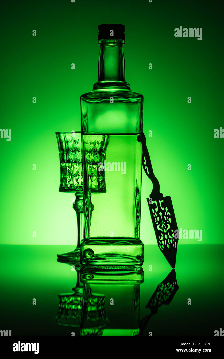 absinthe bottle with crystal glass and spoon on reflective surface and dark green background Stock Photo