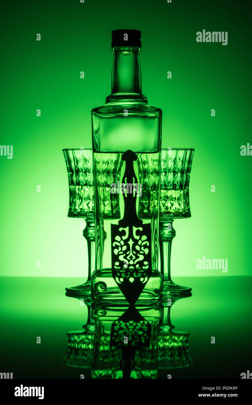 bottle of absinthe with crystal glasses on reflective surface and dark green background Stock Photo
