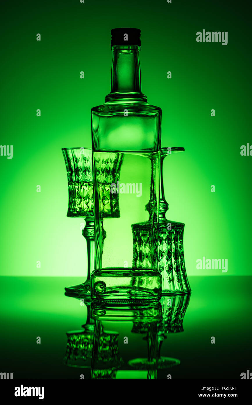 bottle of absinthe with lead glasses on reflective surface and dark green background Stock Photo