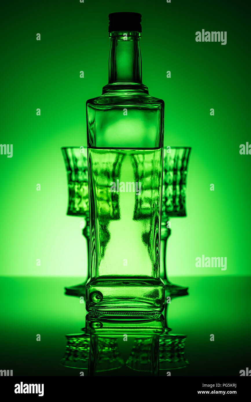 bottle of absinthe with glasses on mirror surface and dark green background Stock Photo