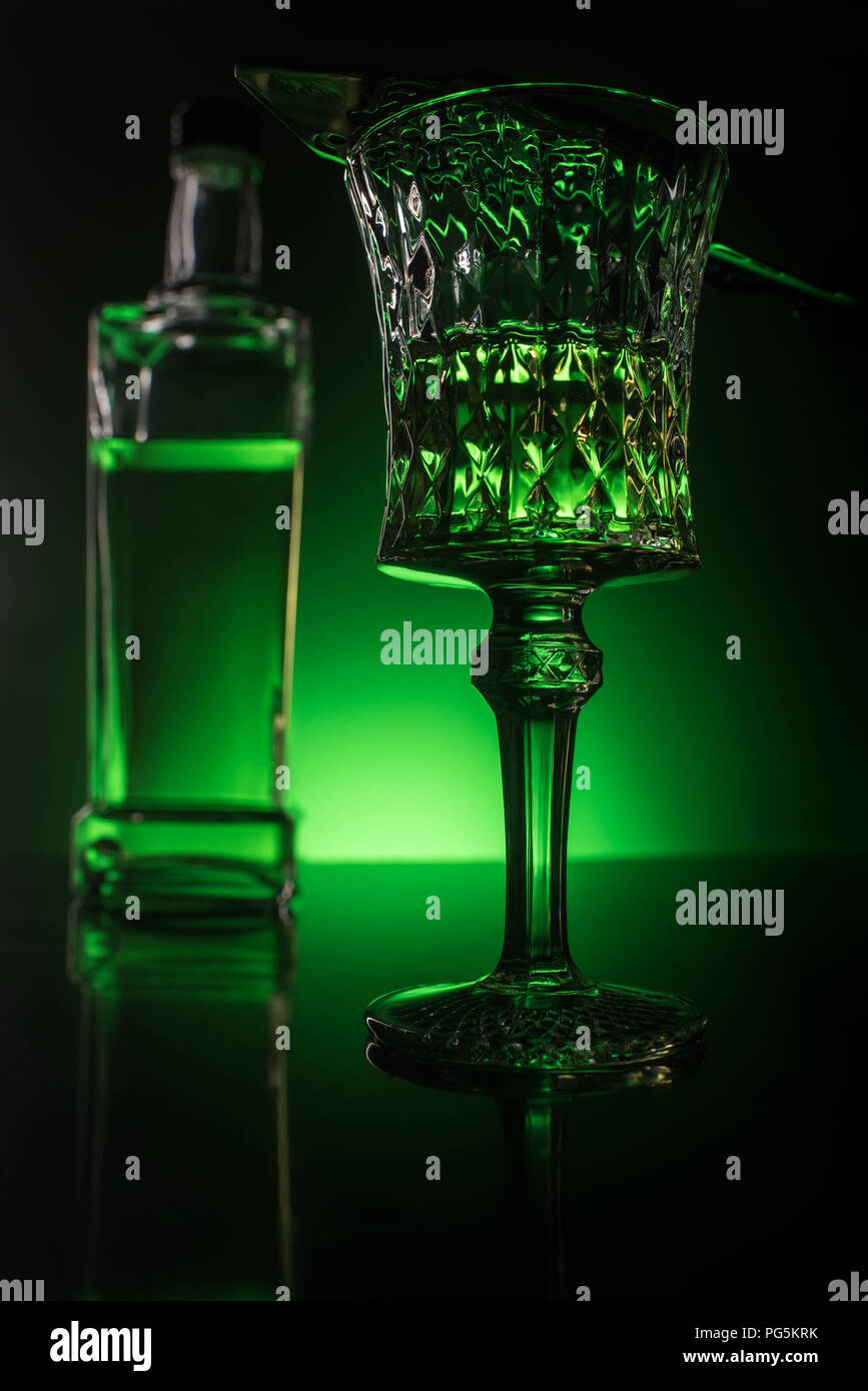 close-up shot of glass with absinthe and bottle on reflective surface and dark green background Stock Photo