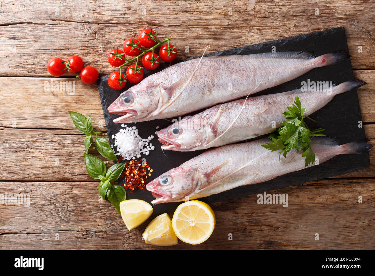 Raw Mediterranean Phycis phycis, or forkbeard fish for cooking with spices, vegetables ingredients close-up on the table. horizontal top view from abo Stock Photo