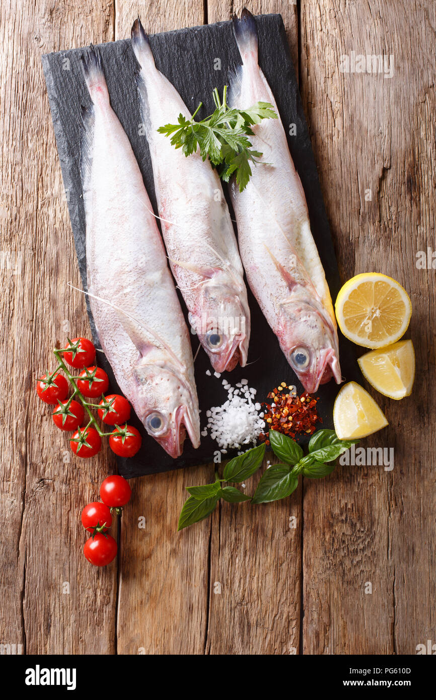 Raw Mediterranean Phycis phycis, or forkbeard fish for cooking with spices, vegetables ingredients close-up on the table. Vertical top view from above Stock Photo