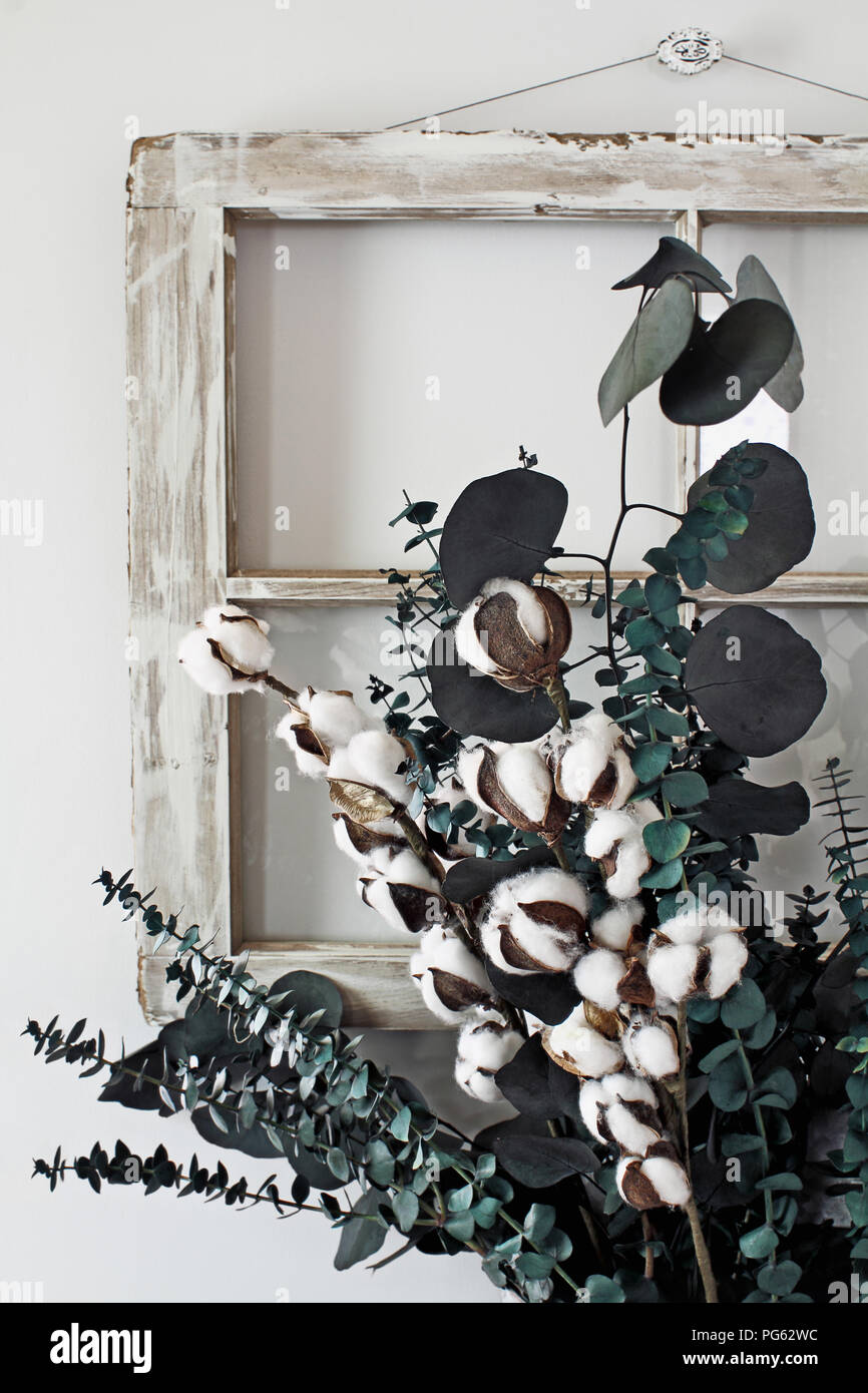 Eucalyptus and cotton stem arrangement in front of an old farmhouse window. Stock Photo