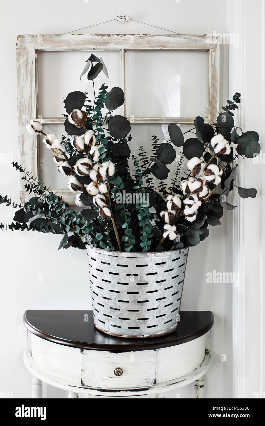Note to reviewer. Items are all generic. Old olive bucket filled with eucalyptus and cotton stem arrangement on a farmhouse table in front of vintage  Stock Photo