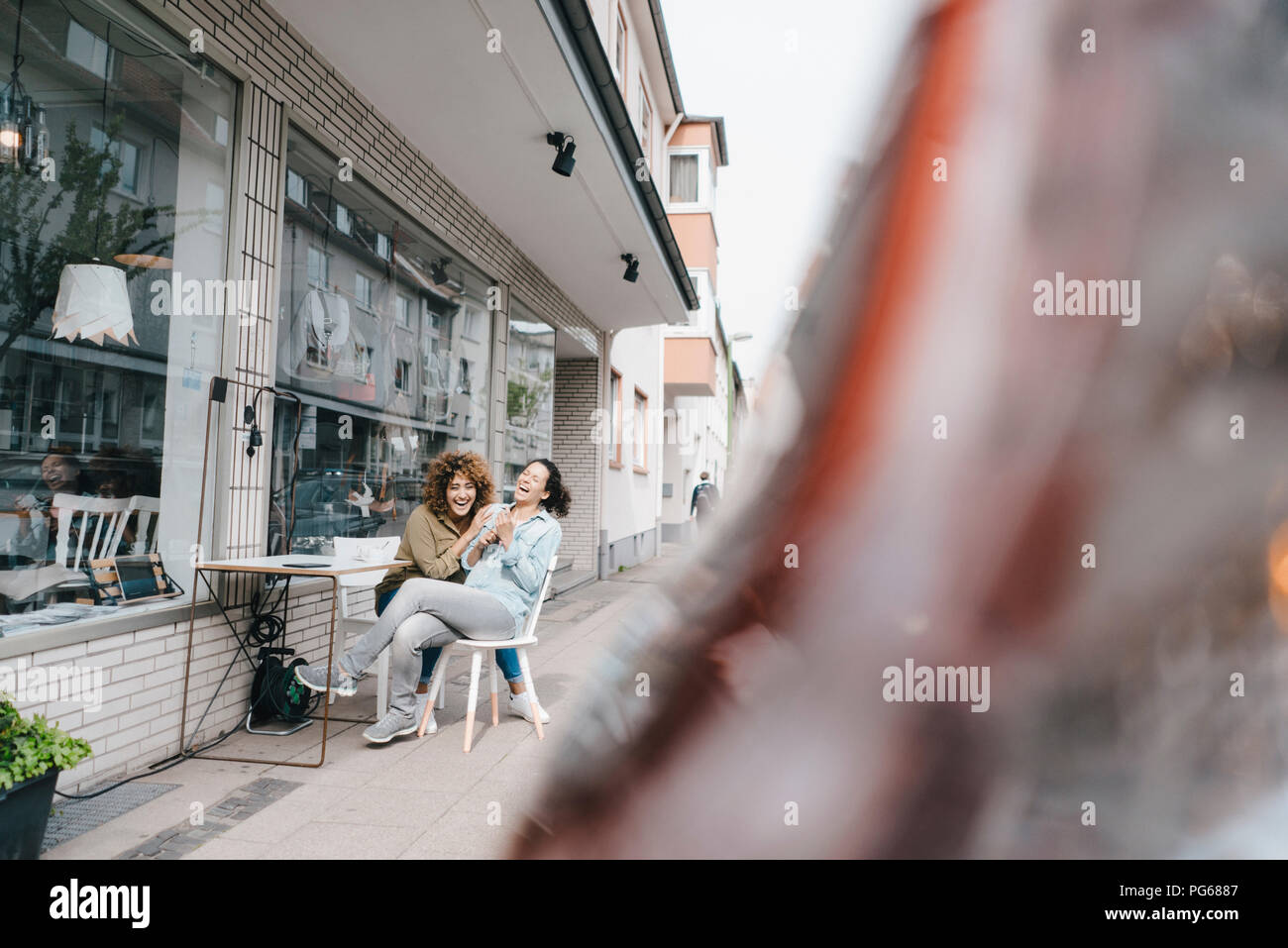 Two laughing friends sitting in front of coworking space Stock Photo