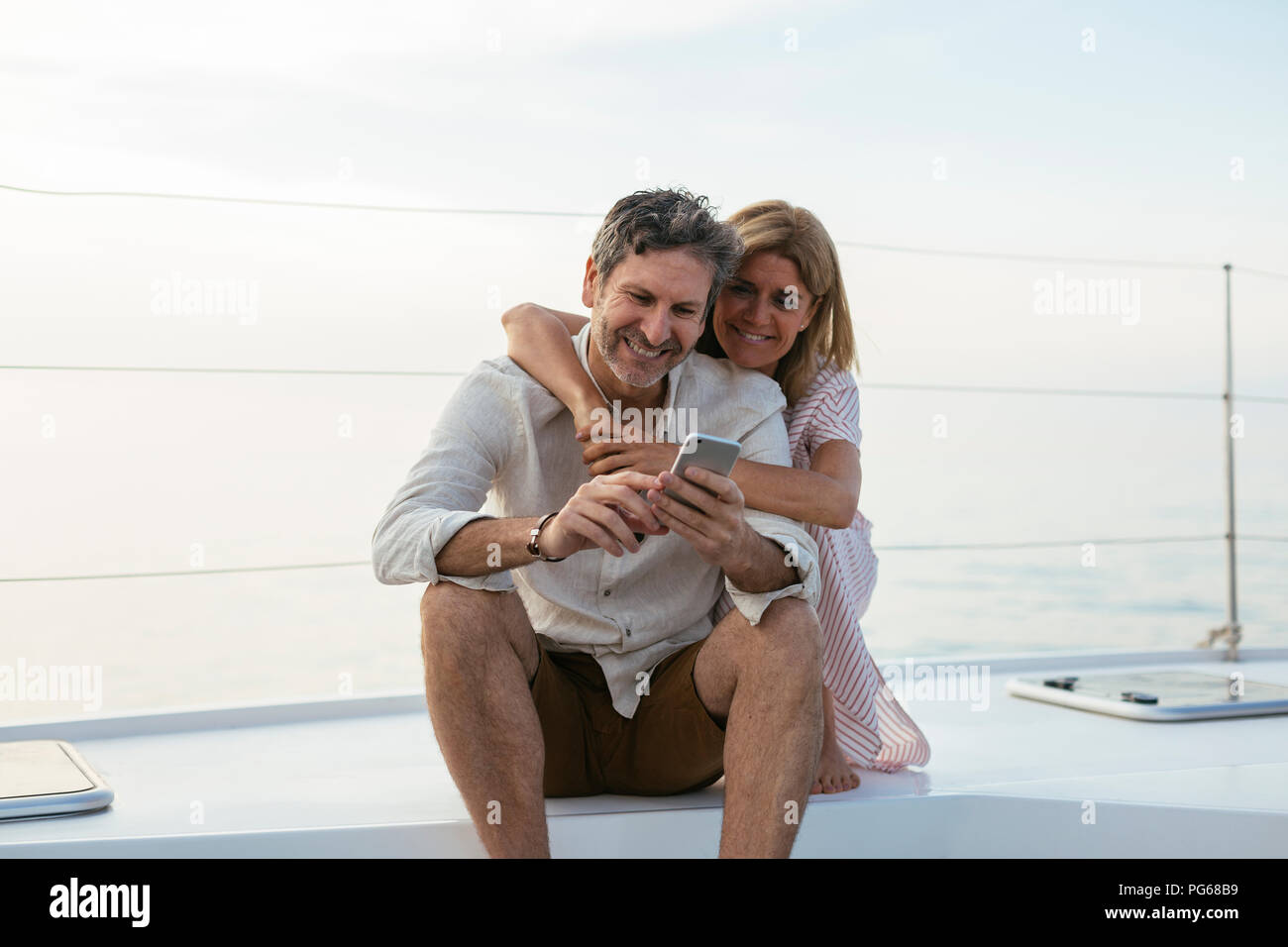 Mature couple looking at smartphone, sitting on a sailing boat Stock Photo