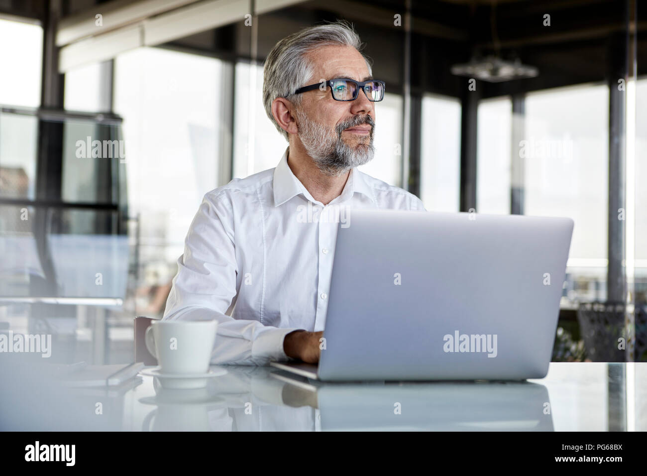 Businessman with laptop at desk in office thinking Stock Photo