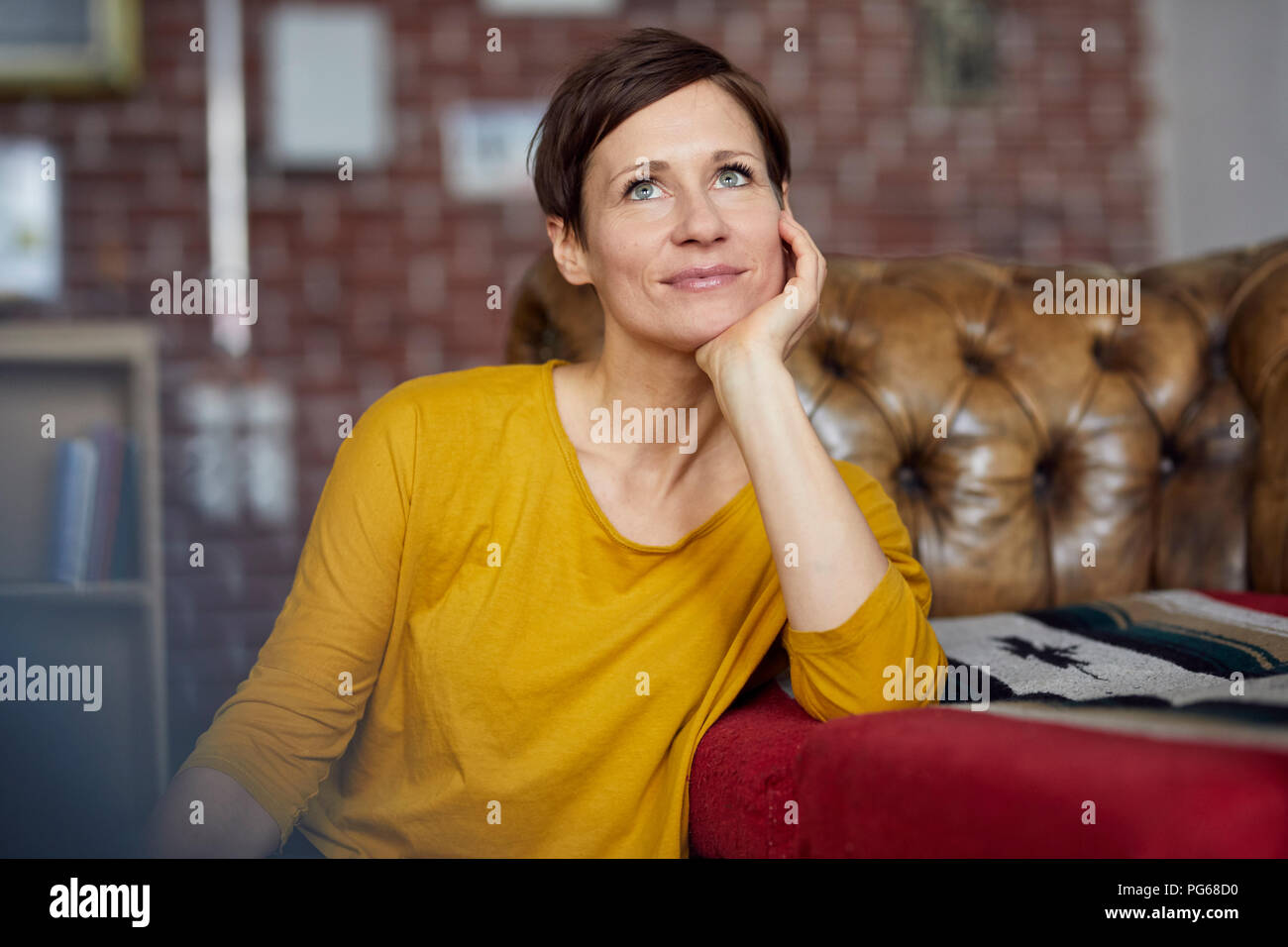 Attractive woman sitting at home with hand on chin Stock Photo - Alamy
