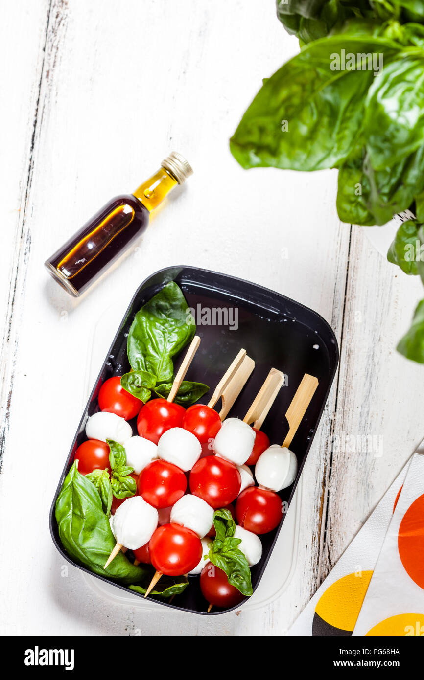 Lunch box of skewered cherry tomatoes and mozzarella cheese balls with basil leaves Stock Photo