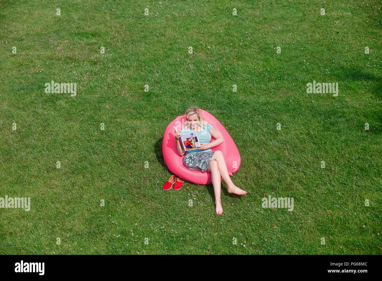 Woman sitting in inflatable seat on meadow looking at photo book Stock Photo