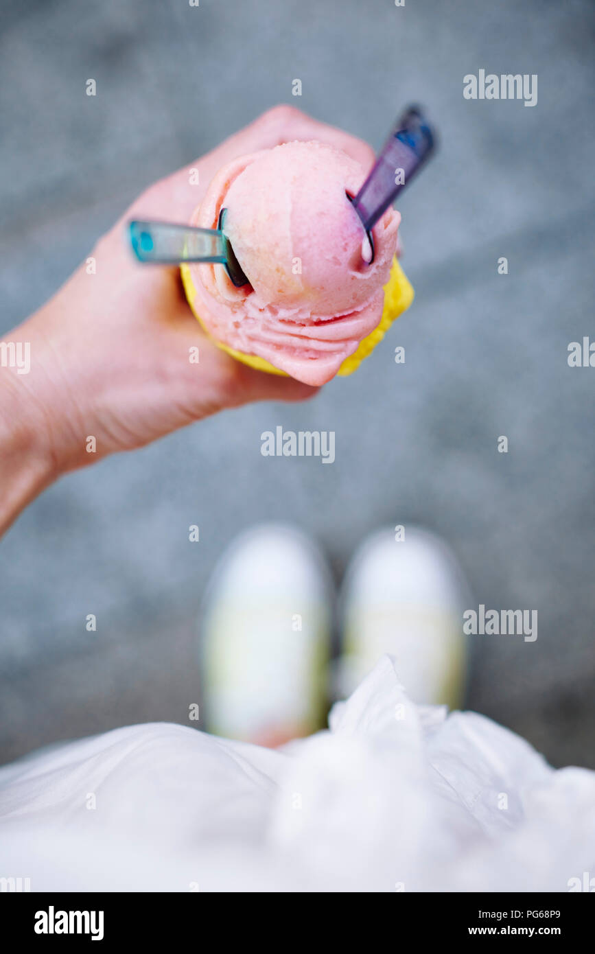 Woman's hand holding ice cream cone with two scoops and spoons Stock Photo