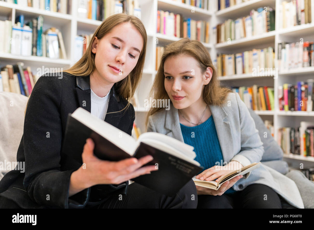 Portrait of two teenage girls sitting  in a public library looking at a book Stock Photo