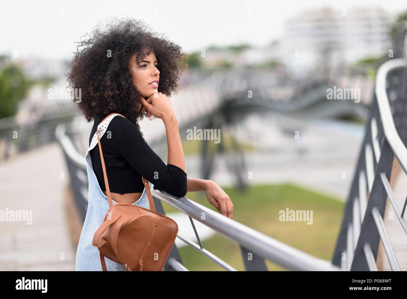 Young woman with brown leather backpack standing on a bridge looking at distance Stock Photo