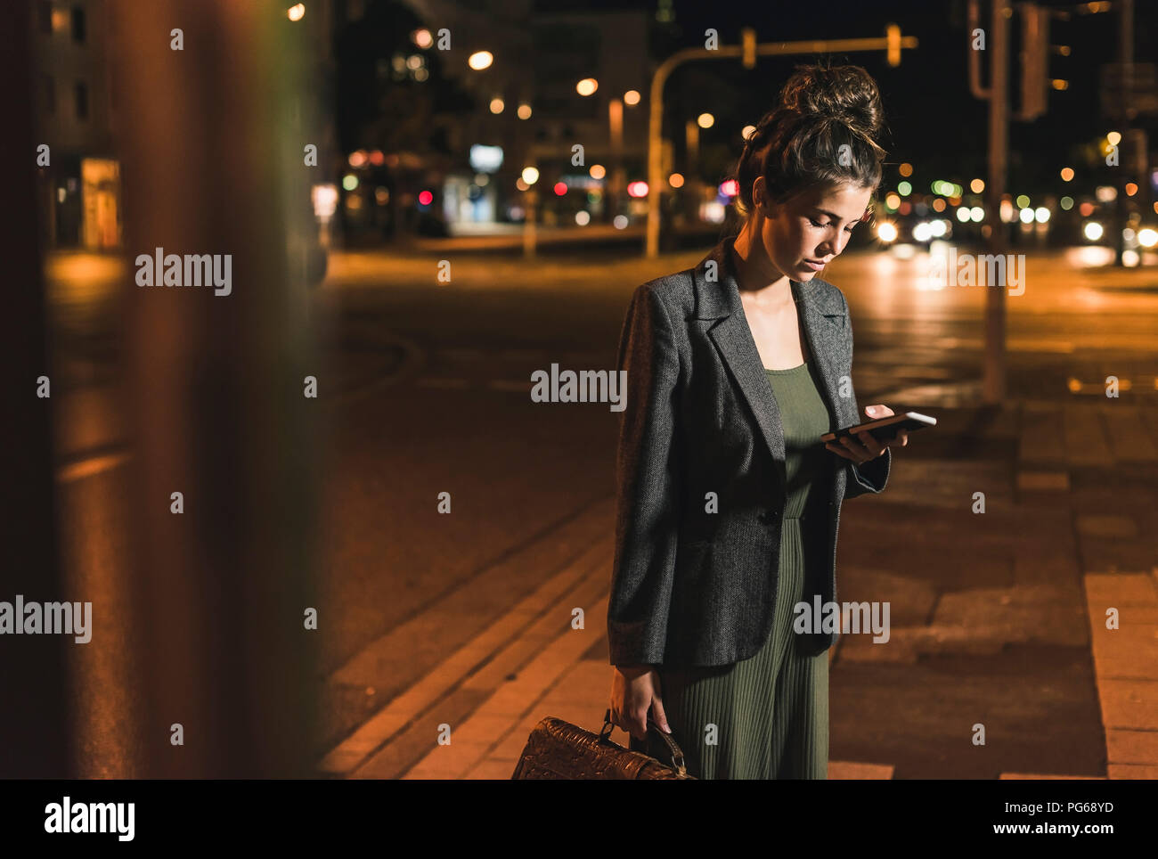 Young businesswoman with leather bag looking at cell phone by night Stock Photo
