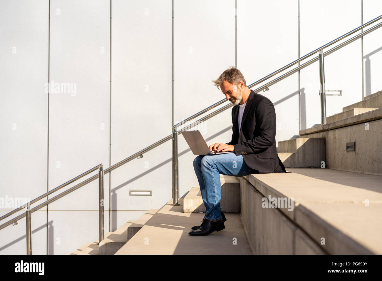 Businessman sitting on steps outdoors using laptop Stock Photo