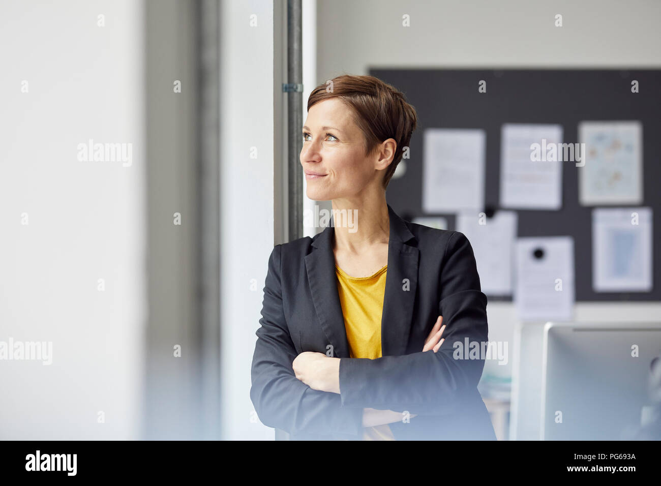 Attractive businesswoman standing in office with arms crossed Stock Photo