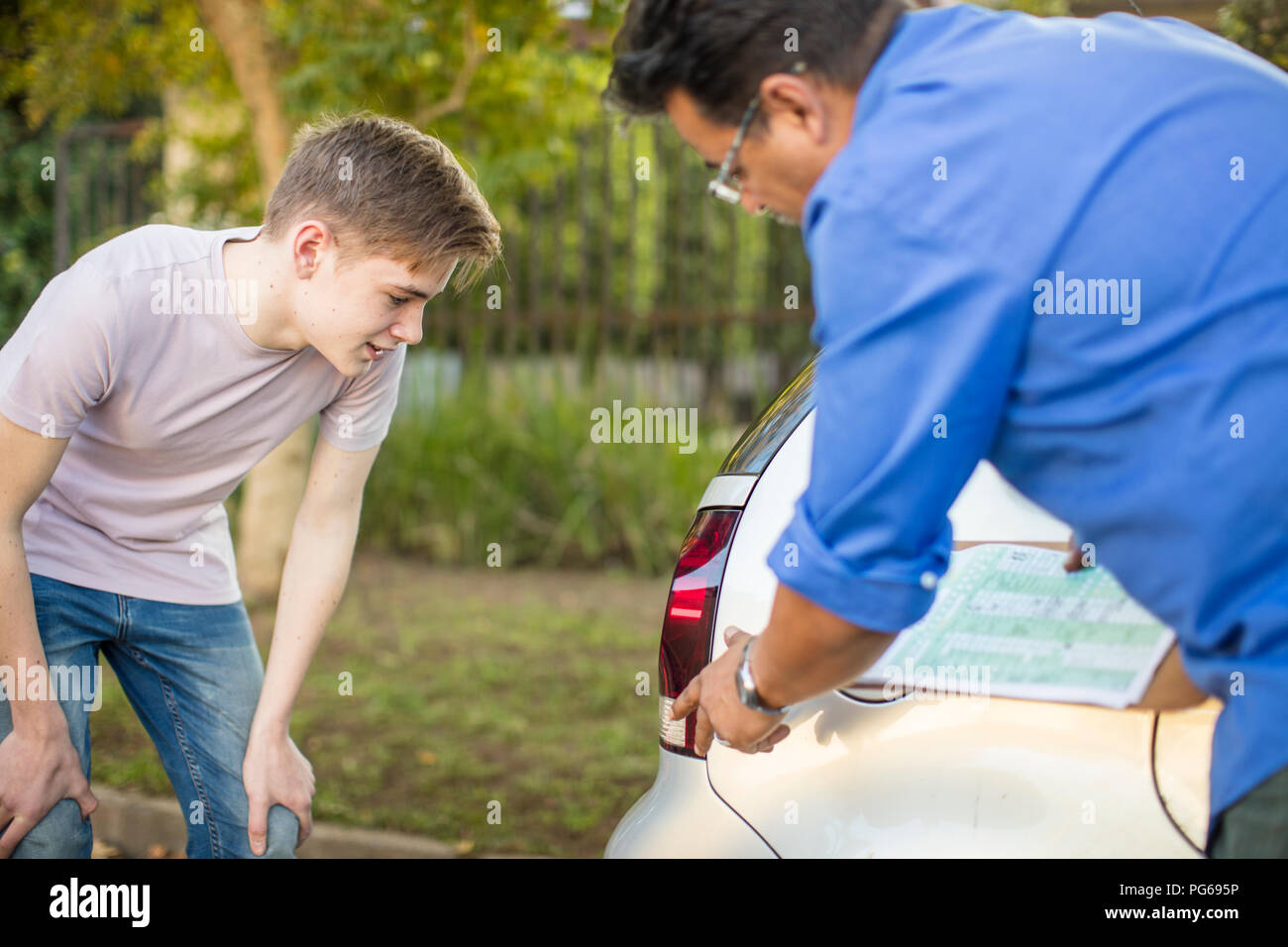 Learner driver with instructor checking rear light of a car Stock Photo
