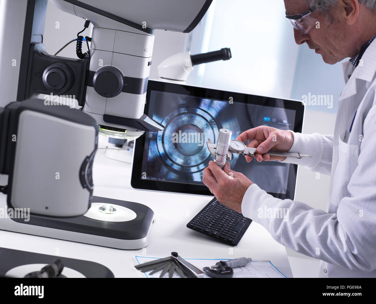 Engineer using a dial calliper and a 3d stereo microscope for quality control in the manufacturing of engineering components for industry Stock Photo