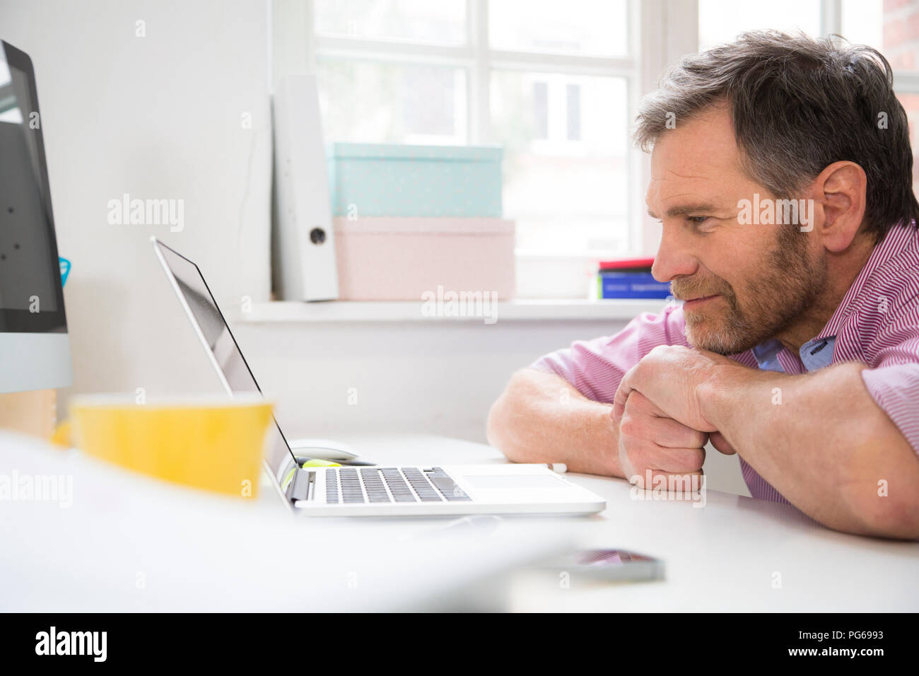 Smiling man leaning on desk in office using tablet Stock Photo