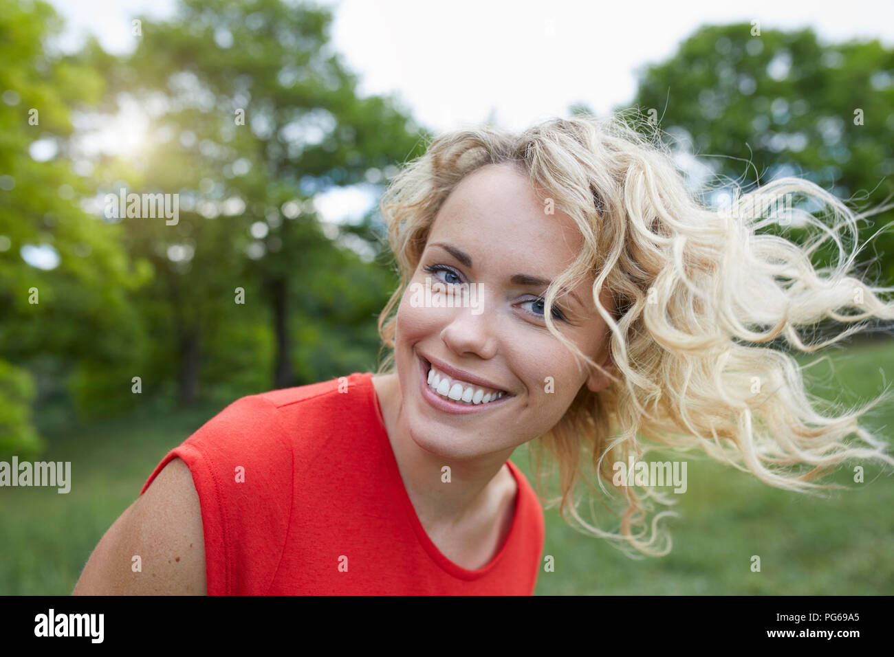 Portrait of smiling blond woman  wearing red t-shirt outdoors Stock Photo