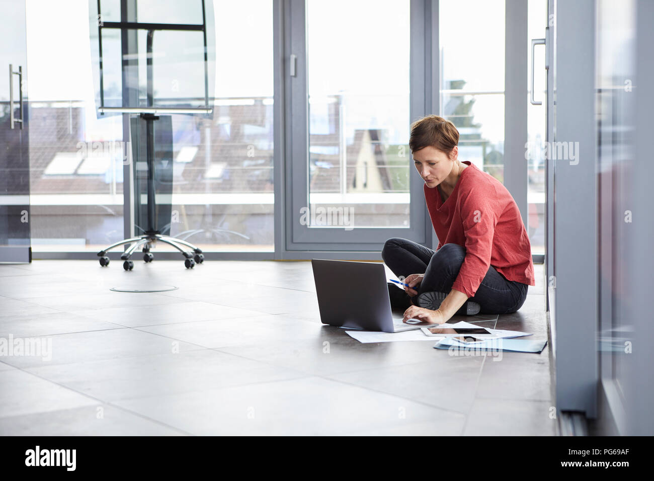 Businesswoman sitting on the floor in office using laptop Stock Photo