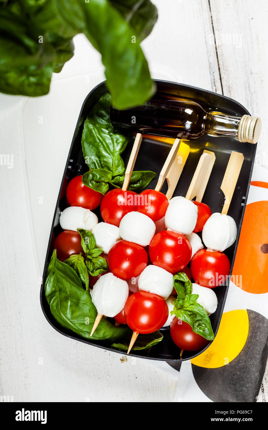 Lunch box of skewered cherry tomatoes and mozzarella cheese balls with basil leaves and vinaigrette Stock Photo