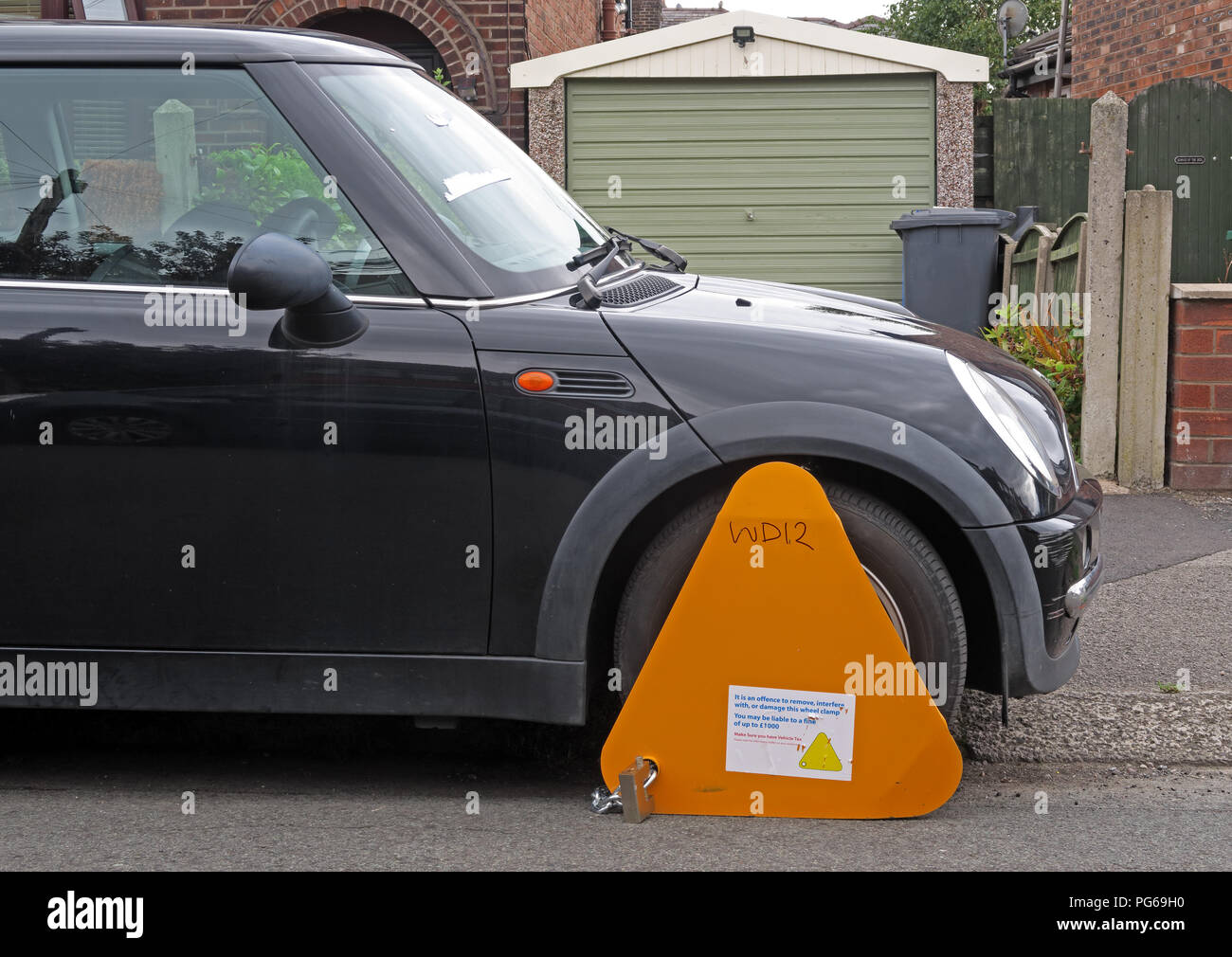 Orange DVLA clamp, immobilising a black mini vehicle, where UK car tax has not been paid, Grappenhall, Warrington, Cheshire, North West England, UK Stock Photo