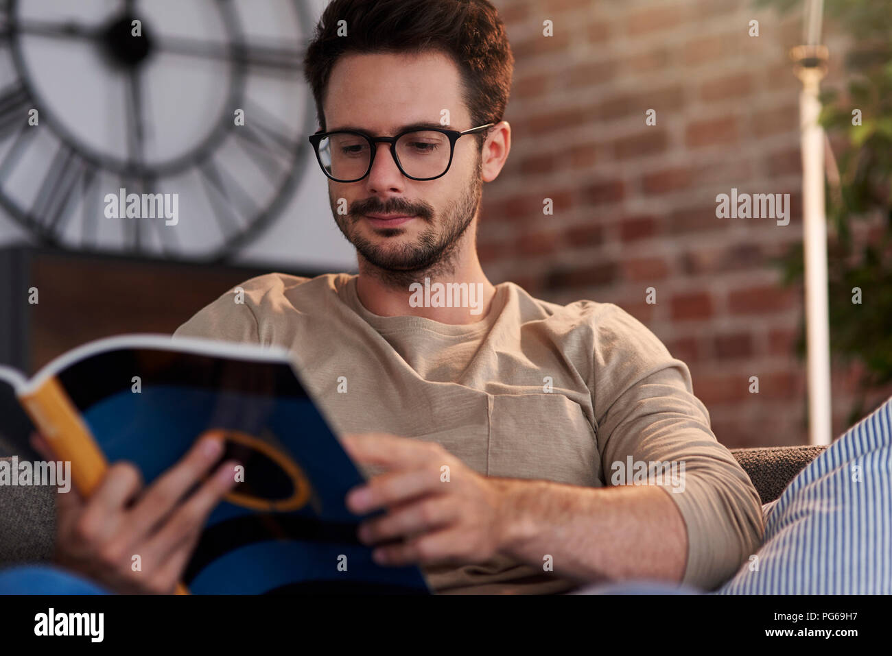 Portrait of man sitting on couch at home reading a book Stock Photo