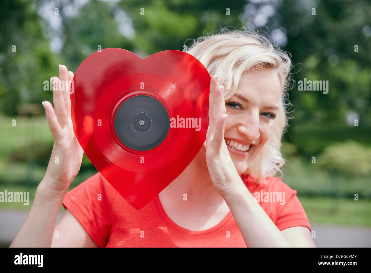 Portrait of happy woman holding a heart-shaped vinyl record outdoors Stock Photo