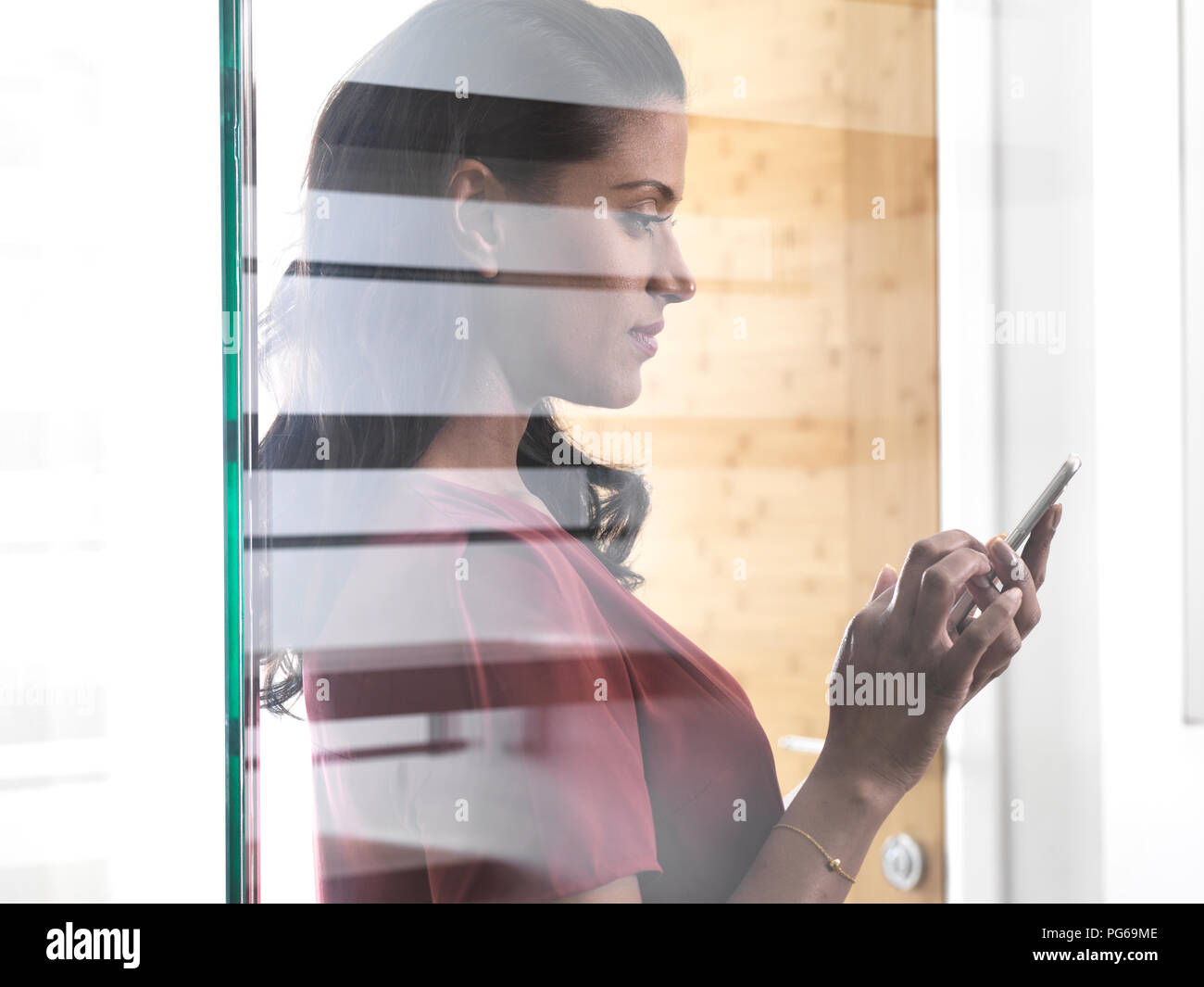 Profile of woman behind glass pane using smartphone Stock Photo