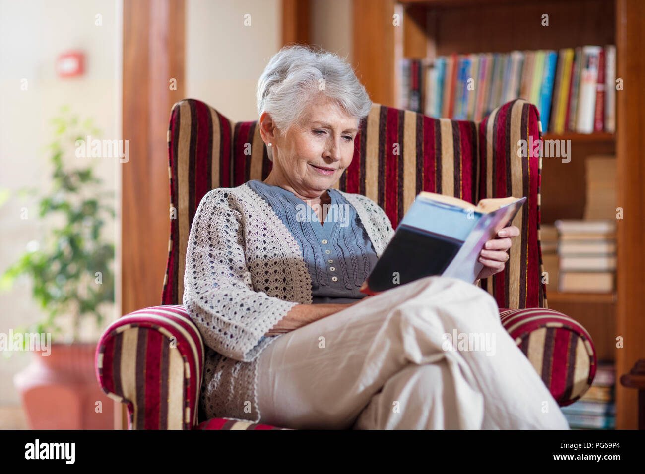 Senior woman siting in library, reading book Stock Photo