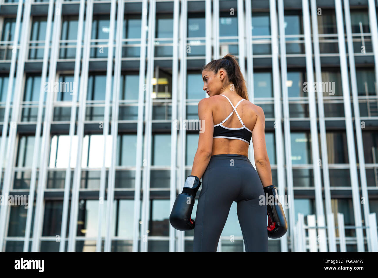 Sportive young woman with boxing gloves in the city in front of a high-rise building Stock Photo