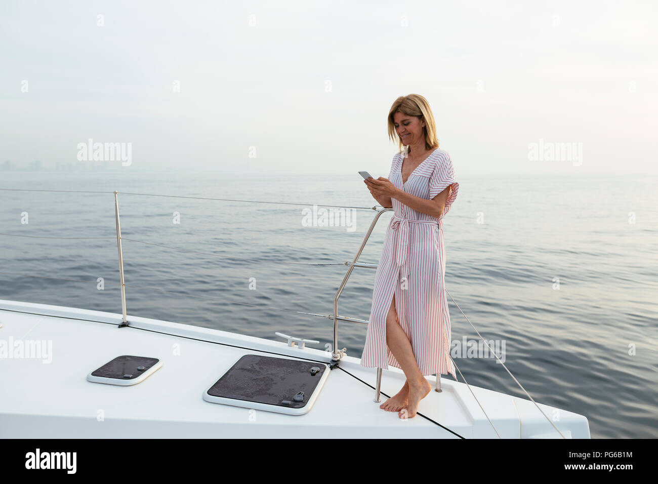 Mature woman standing on catamaran, using smartphone Stock Photo