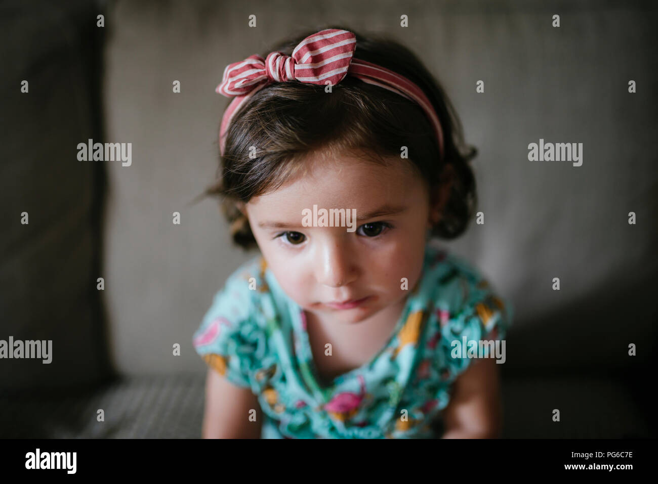 Baby girl sitting on the couch at home, hair band Stock Photo