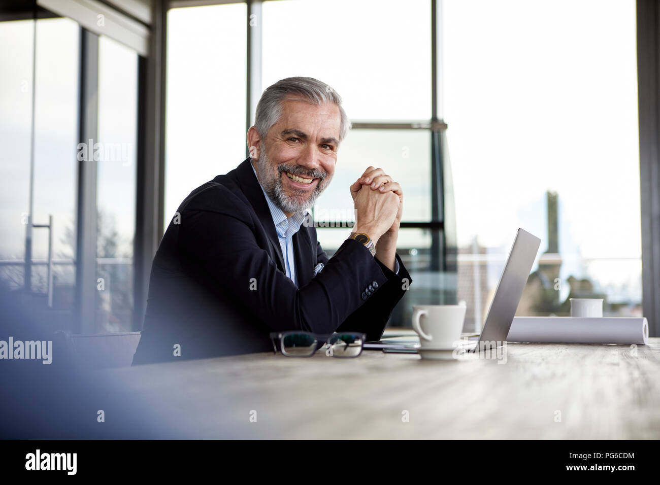 Portrait of smiling businessman with laptop at desk in office Stock Photo