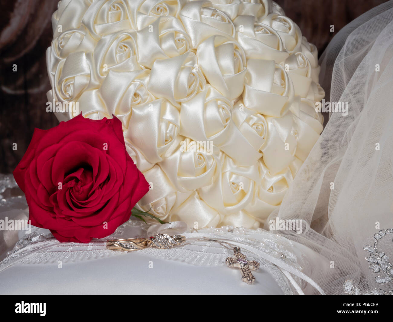 Bride's bouquet with veil, red rose, wedding rings & cross on ring bearer's pillow Stock Photo