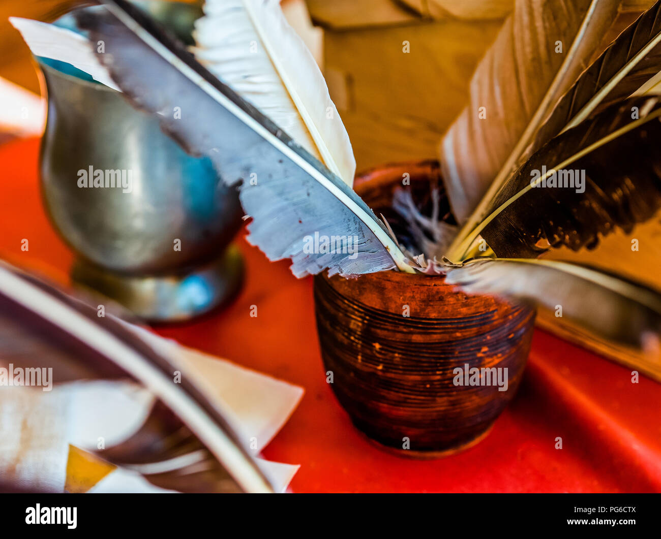 Ceramic bowl full of ancient quills stands on a table covered with a red tablecloth. Metal bowl in the background. Back to school, white a message the Stock Photo