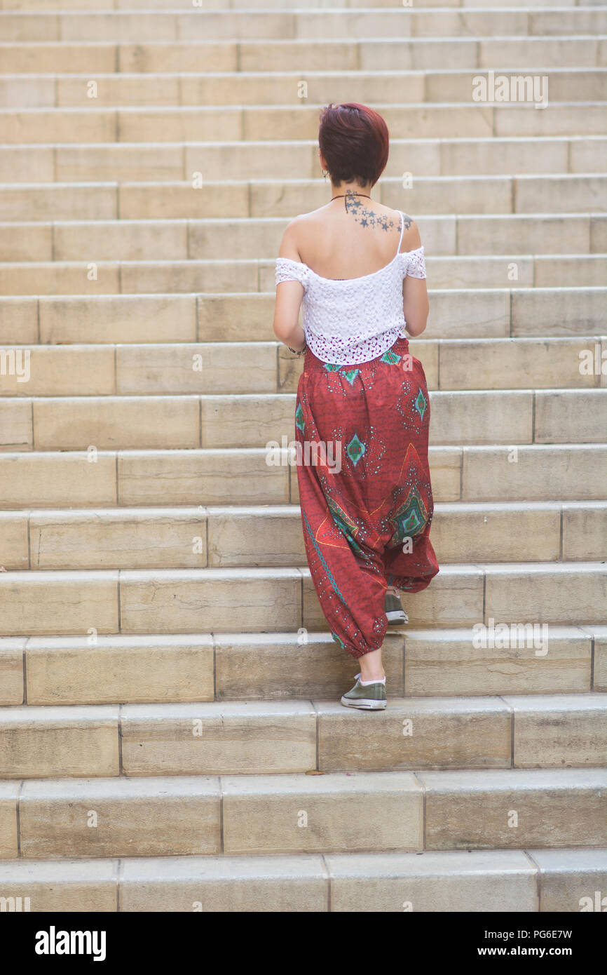 Rear view of a young woman wearing harem pants walking up the stairs outdoors Stock Photo