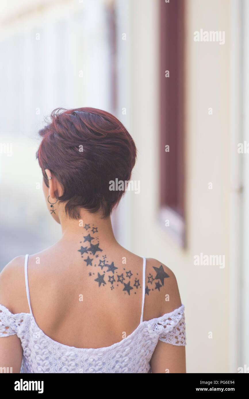 Rear view of a young woman with short red hair and stars tattoo on back standing outdoors Stock Photo