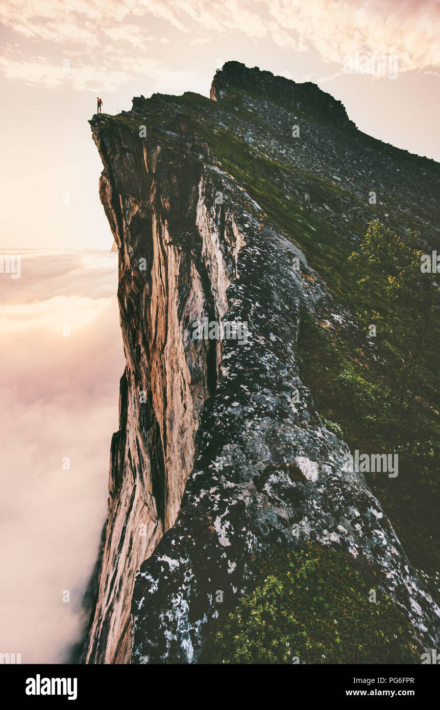 Man standing on cliff edge mountain ridge above sunset clouds travel adventure lifestyle summer journey vacations Stock Photo