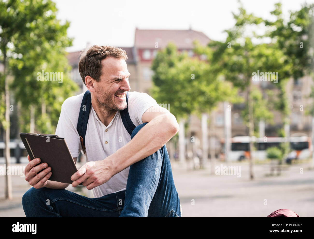 Smiling man sitting outdoors with tablet Stock Photo